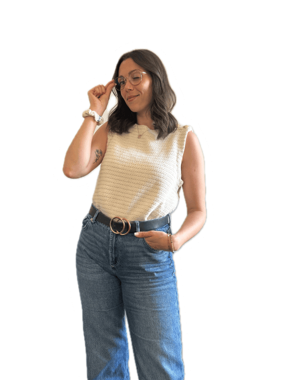 Femme avec lunettes et débardeur beige, main sur la taille, regard complice vers le haut.