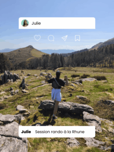 Femme de dos sur un sentier de randonnée en montagne, levant les bras en signe de victoire face à un paysage de crêtes et de vallées verdoyantes.