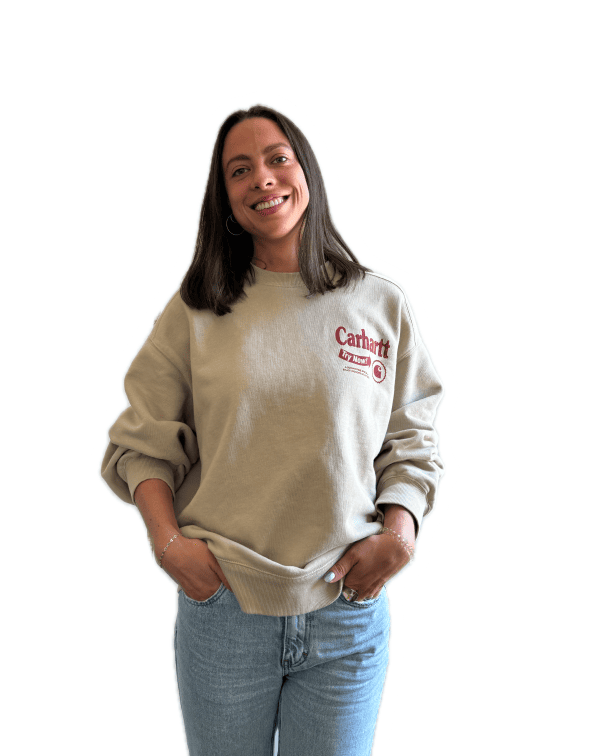 Femme en sweat beige et jean, souriante et détendue, mains dans les poches.
