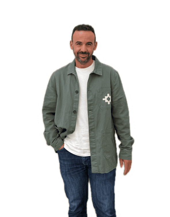 Homme debout en veste verte et t-shirt blanc, posture détendue avec un léger sourire.