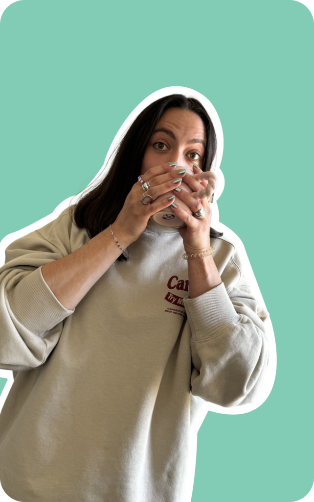 Jeune femme portant un sweat beige décontracté boit une tasse qu'elle tient avec ses deux mains et arbore un air étonné.